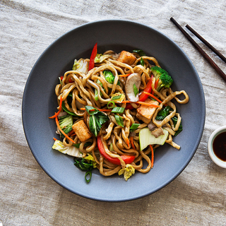 black bowl with vegetable and tofu lo mein with wooden chopsticks and a dish of soy sauce