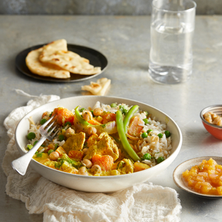 Vegetarian yellow coconut curry in a white bowl on a white table with naan on a black plate in the background