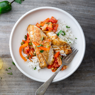 cod fillet with roasted vegetables and white rice on a white dinner plate with a sliced jalapeno pepper on the side