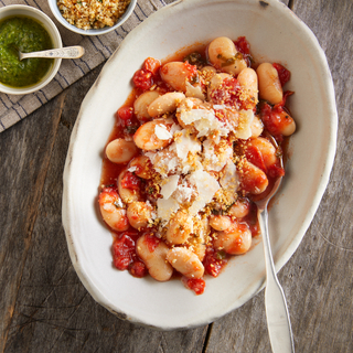 White bean gratin with tomato sauce and shaved cheese ina white bowl on a wooden table. 