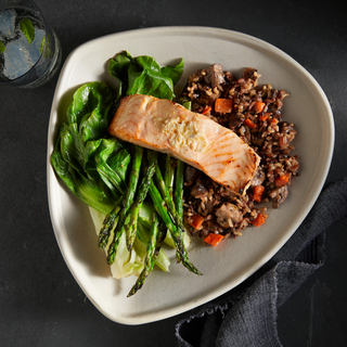 White dinner plate with wild rice salad, grilled bok choy and asparagus with white miso roasted salmon fillet. 