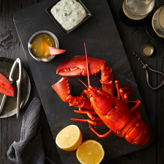 whole red lobster on a black plate with melted butter, tartar sauce and a lemon sliced in half