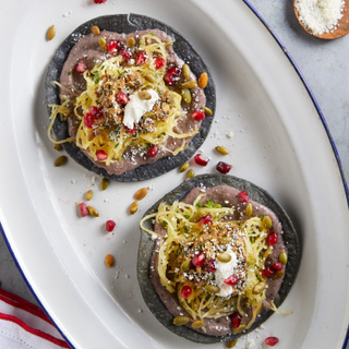 Two winter squash panuchos with sour cream and pumpkin seeds and pomegranate seeds on a white platter with a blue rim