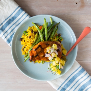 Yucatan Adobo Pork on a light blue plate with rice, beans and grilled pineapple salsa on a light wood surface 
