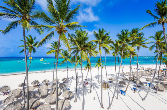 Beautiful white sand beach in Punta Cana with tall palm trees, thatched umbrellas, and clear turquoise ocean water