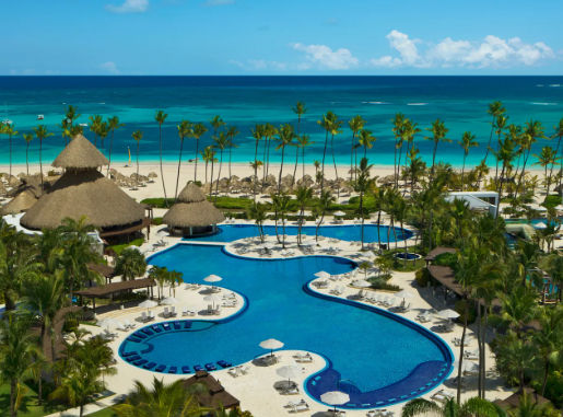 Aerial view of a luxury tropical resort with a winding blue pool, white sand beach, and palm trees