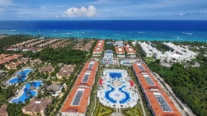 Aerial view of a large tropical beachfront resort complex with swimming pools and red-roofed buildings.