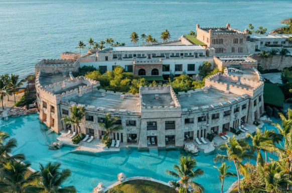 Aerial view of a luxury castle-style beachfront resort with winding pools and palm trees
