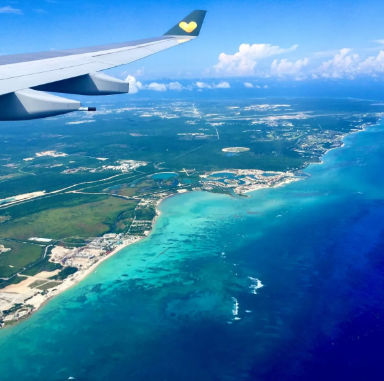 Aerial view from an airplane window flying over a beautiful tropical coastline with turquoise water and beach resorts