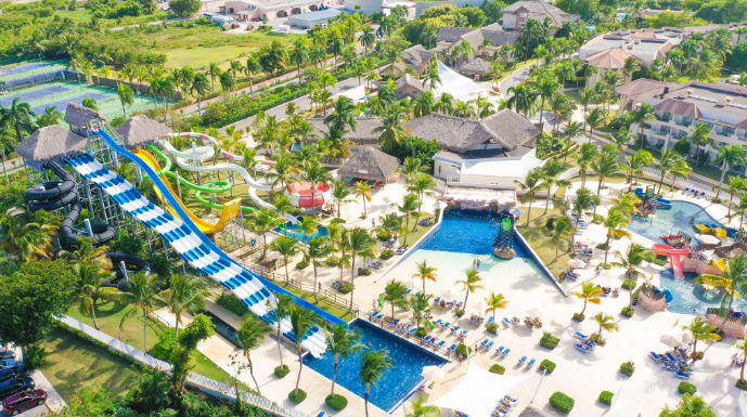 Aerial view of a large tropical resort water park with a multi-slide complex, children's play area, multiple pools, and palm trees.