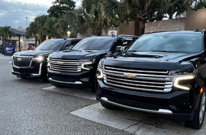 Fila de tres SUVs de lujo negros (Chevrolet y Cadillac) estacionados para servicios de transporte privado frente a un hotel.