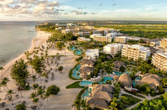 Aerial view of a luxury beachfront resort with large swimming pools, palm trees, and a white sand beach at sunset