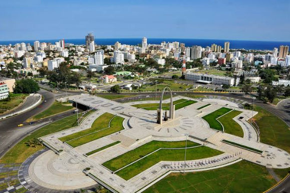 Vista aérea de la Plaza de la Bandera y el Arco del Triunfo en Santo Domingo, con la ciudad y el mar Caribe de fondo.