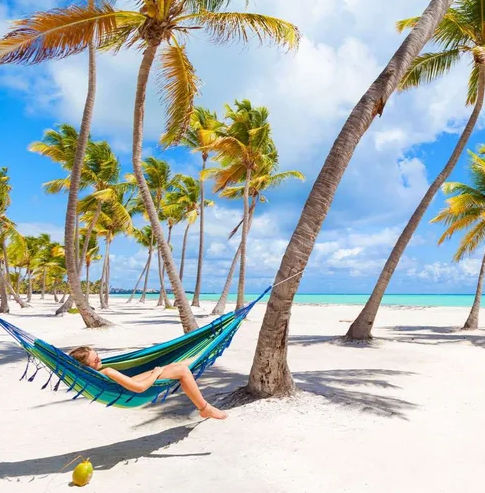Woman relaxing in a colorful hammock on a pristine white sand beach with palm trees and turquoise ocean in Punta Cana, Dominican Republic