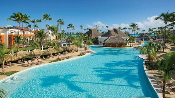 gran piscina exterior de un complejo turístico tropical con palmeras y cabañas de paja