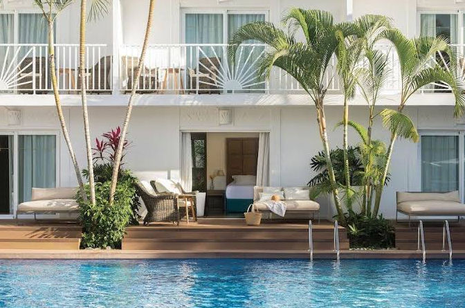 Luxury resort swimming pool with palm trees, lounge chairs, and ground floor suites