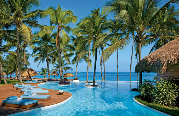 Luxury tropical resort infinity pool with blue lounge chairs and palm trees overlooking the ocean