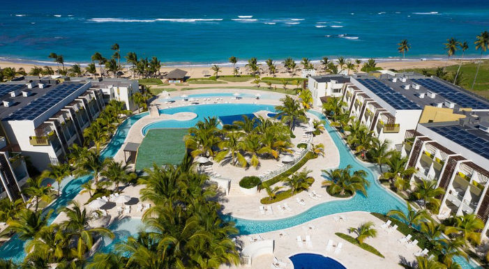 Aerial view of a modern solar-powered tropical beach resort with multi-tiered complex swimming pools, lounge chairs, and ocean views