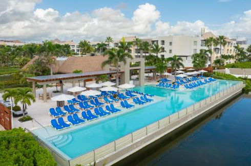 Luxury resort swimming pool with blue lounge chairs, white umbrellas, and tropical palm trees