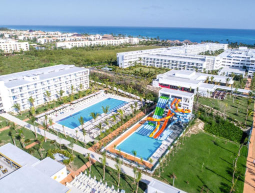 Aerial view of a beachfront resort with swimming pools, colorful water slides, and ocean background