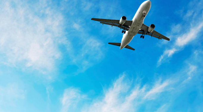 A view from below of a passenger airliner with landing gear deployed, against a bright blue sky and clouds.