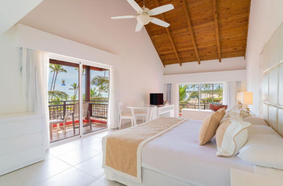 Spacious tropical resort suite with a wooden vaulted ceiling, large bed, and a balcony offering ocean views