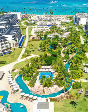 Aerial photograph of a large tropical resort complex with multiple pools, palm trees, modern buildings, and a beach on the ocean.