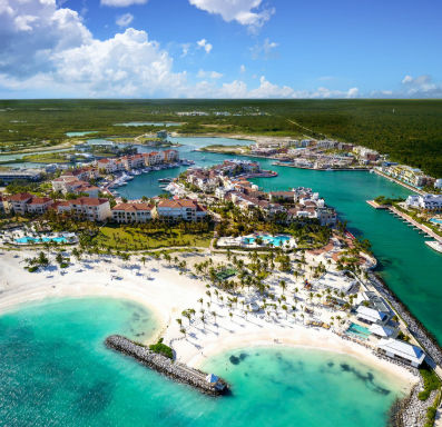 Aerial view of a luxury coastal resort and marina featuring pristine white sand beaches, clear turquoise waters, and palm trees