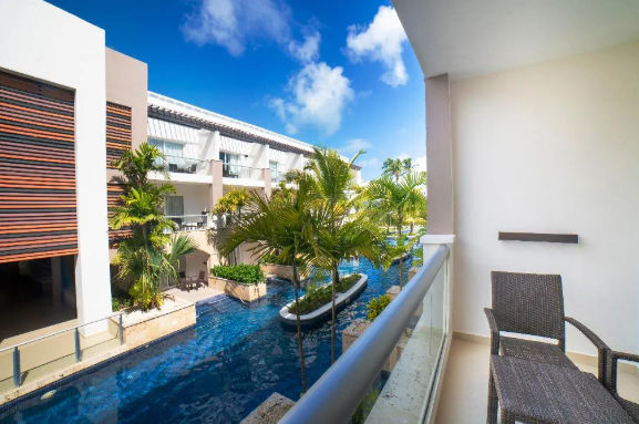 Balcony view overlooking a luxury tropical resort with swim-out pools and palm trees under a sunny blue sky