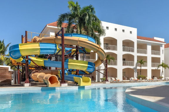 Colorful yellow and blue water slide ending in a clear swimming pool at a tropical resort