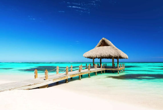 Wooden pier leading to a thatched palapa over bright turquoise water on a tropical beach