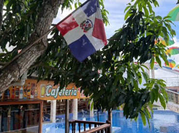 Dominican Republic flag hanging from a tree above an outdoor cafeteria and swimming pool.