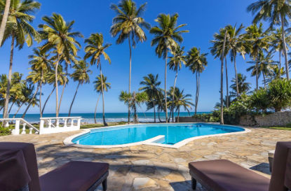 Complejo turistico de Las Canas Beach Retreat con edificios blancos rodeados de palmeras, jardines verdes y una zona de hoguera frente al mar bajo un cielo despejado
