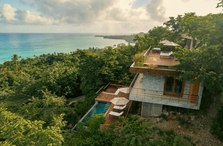 Aerial view of a modern luxury villa at Ocama, Las Galeras, surrounded by dense tropical vegetation with wooden decks, a private pool, and a panoramic view of the Caribbean Sea.
