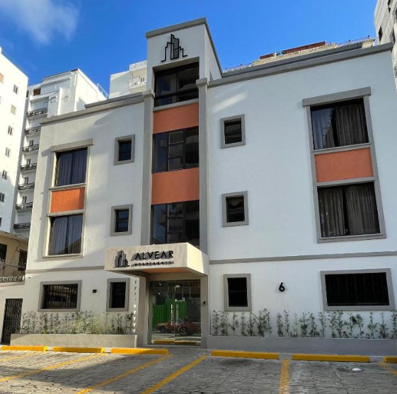 Fachada moderna del Apartahotel Alvear en Santo Domingo, mostrando la entrada principal, estacionamiento frontal y el logotipo del hotel.