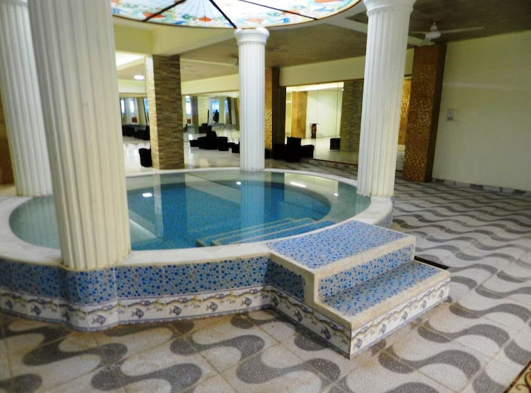 Circular indoor pool or jacuzzi inside the spa area at Hotel Spa Bella Mar, surrounded by classical white columns, blue tiled steps, and wavy patterned flooring.