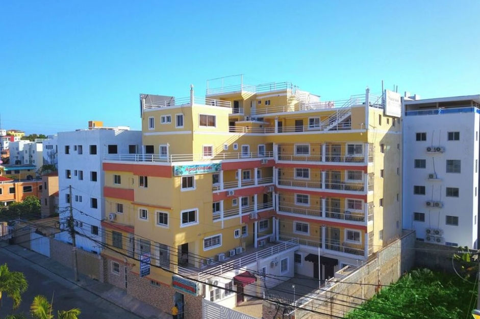 An aerial view of a multi-story yellow and orange aparthotel building under a clear blue sky in Punta Cana
