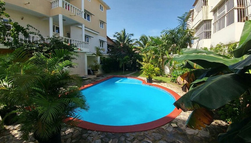 Fachada exterior del Aparthotel Michaela en Sosúa, un edificio de tres niveles con balcones, palmeras y letrero de recepción bajo un cielo azul despejado.