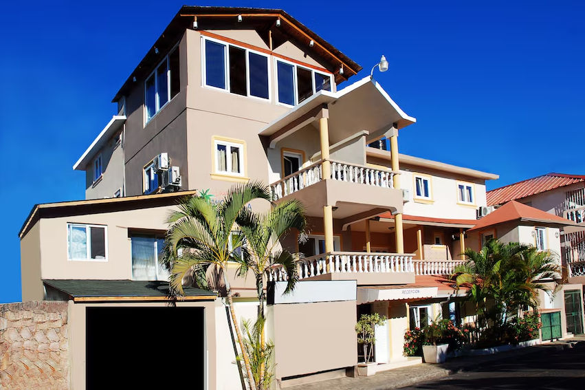 Fachada exterior del Aparthotel Michaela en Sosúa, un edificio de tres niveles con balcones, palmeras y letrero de recepción bajo un cielo azul despejado.