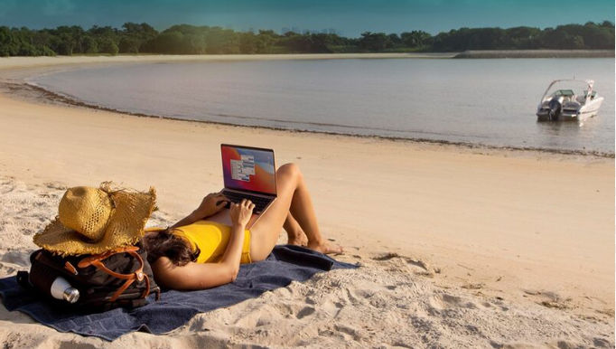 Digital nomad working on a laptop while lying on a sandy beach in the Dominican Republic