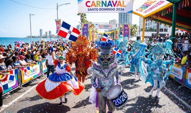 Vibrant parade of the Carnaval Santo Domingo 2026 on the seaside boardwalk with performers in colorful elaborate costumes and waving Dominican flags.