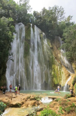 Tall waterfall in Samaná, Dominican Republic, with eco-tourists swimming in the turquoise natural pool at its base.