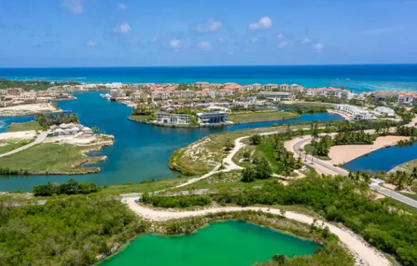 Aerial view of a coastal resort community with vibrant blue canals, lush greenery, a bright green lagoon, and the ocean in the background