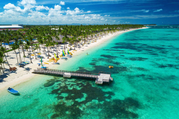 Aerial view of a beautiful tropical beach with turquoise water, palm trees, and a wooden pier in the Dominican Republic