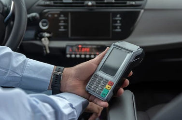 A hand holding a portable credit card payment terminal inside a car.