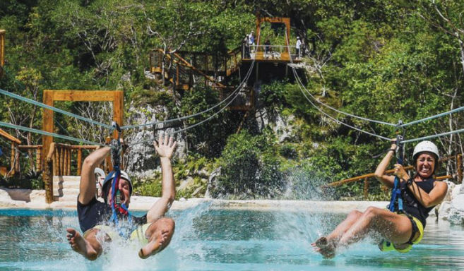 Man and woman splashing into a blue pool while ziplining on a tropical excursion