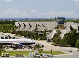 Tropical airport tarmac with a parked airplane, thatched roof terminals, and an air traffic control tower