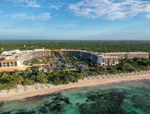 Aerial view of a large curved beachfront resort complex surrounded by lush tropical jungle and ocean