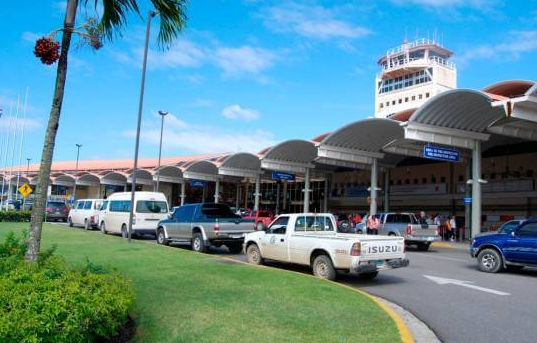 Exterior view of a tropical airport terminal with vans and trucks waiting at the passenger pick up area