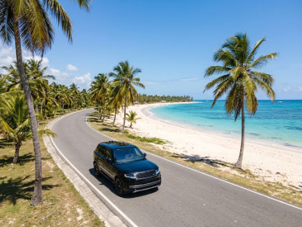 Black private transfer vehicle on a scenic coastal road next to a tropical beach in Punta Cana.